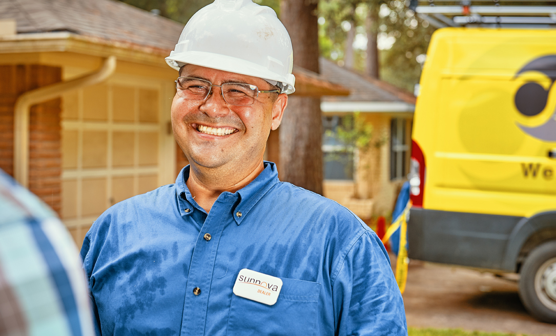 Man wearing hard and blue shirt smiling in front of camera.